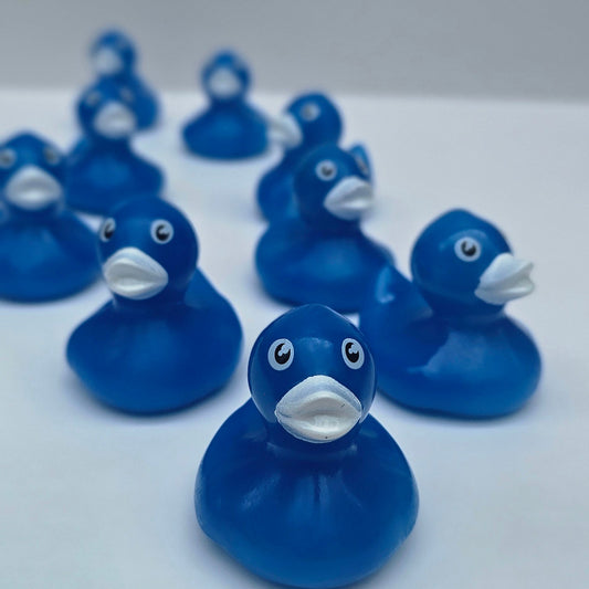A row of small blue rubber ducks with white beaks and black eyes arranged diagonally against a plain light gray wall.