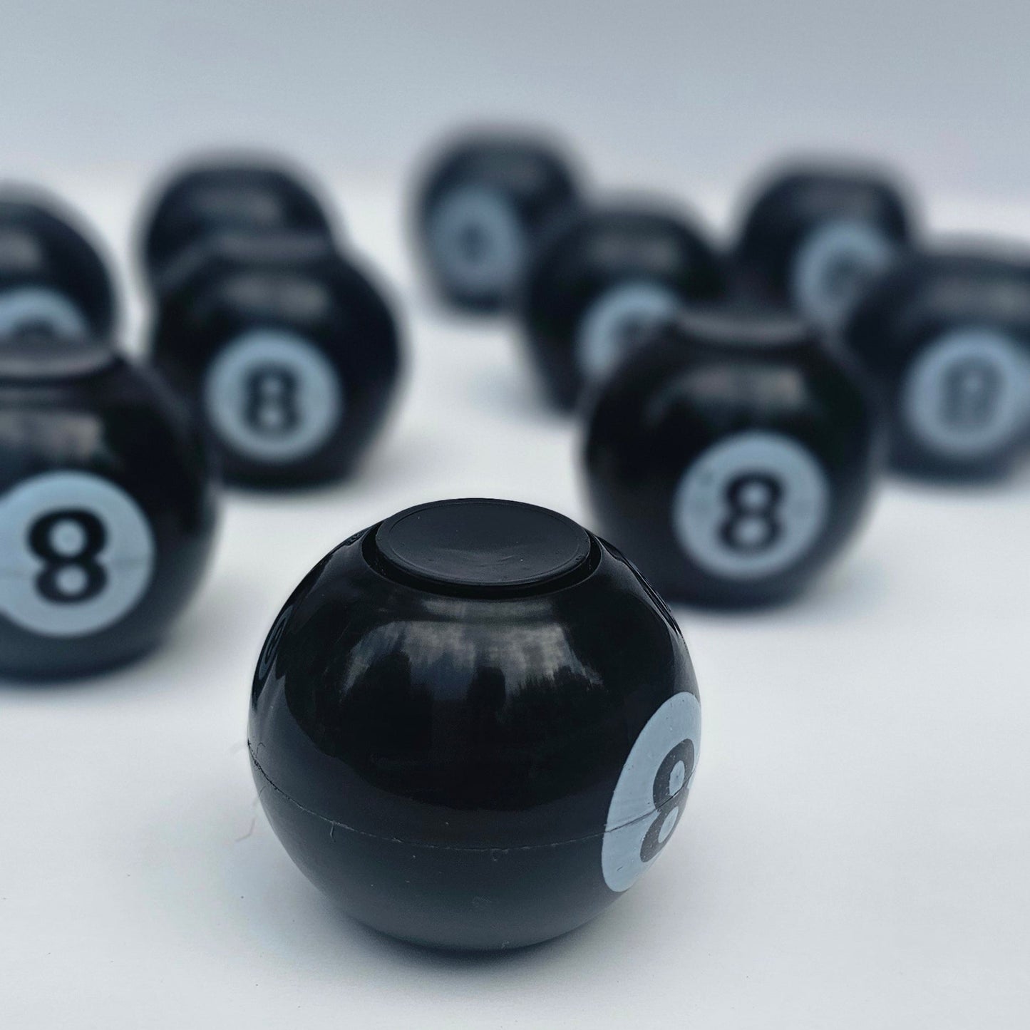 A glossy black 8-ball billiard ball in sharp focus, with several blurred black 8-balls arranged diagonally in the background on a light gray surface.