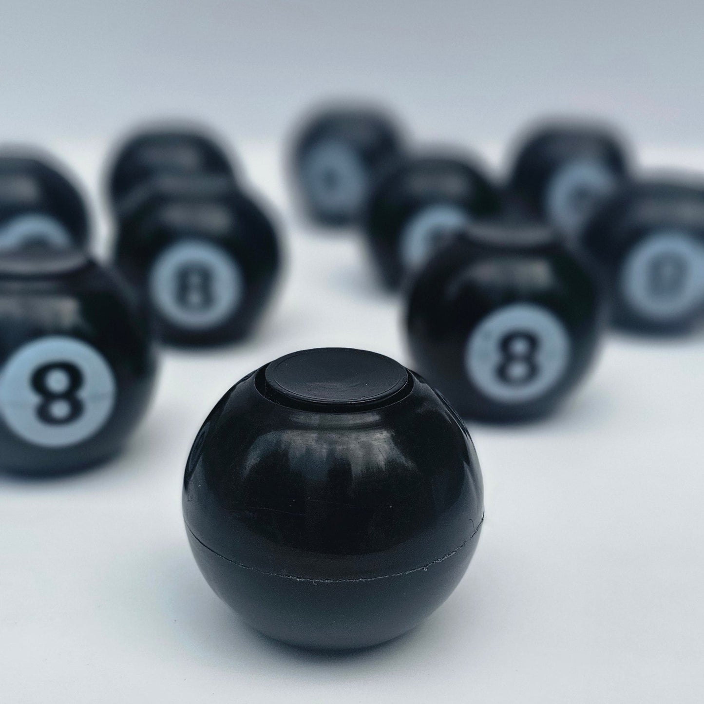 A glossy black 8-ball pool ball in sharp focus, with several blurred black 8-balls arranged diagonally in the background on a light gray surface.