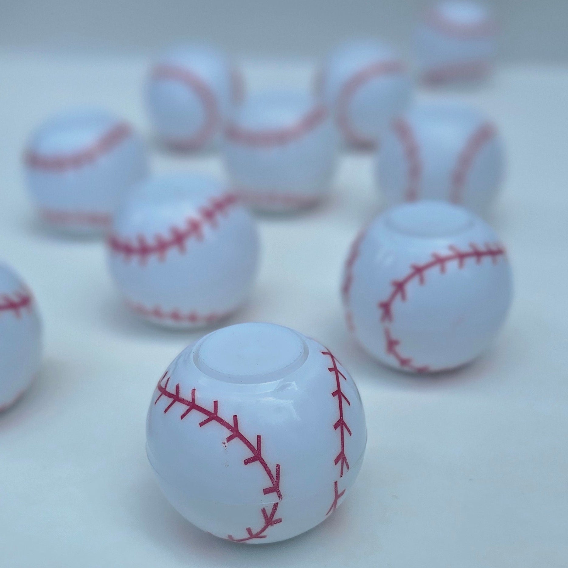 White baseball-shaped spinner balls with red stitching, shown mounted on a light gray wall with several additional hooks blurred in the background.